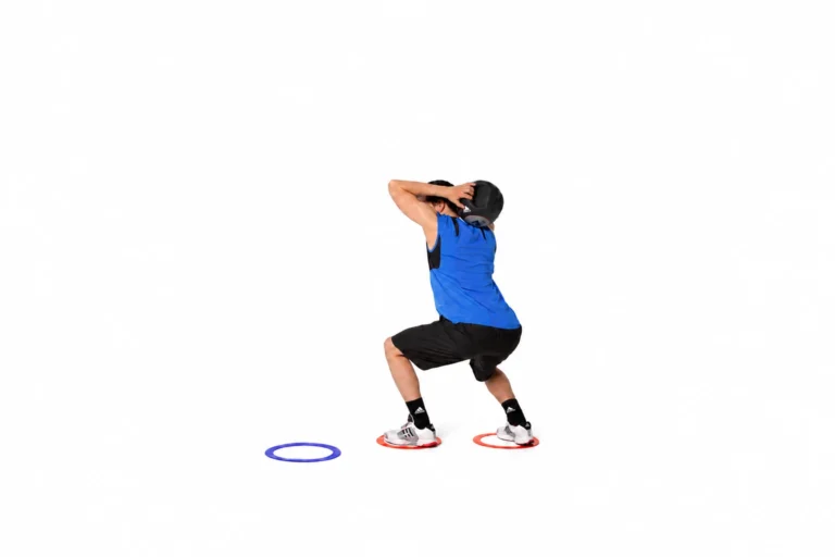 Athlete in the loaded service stance with a medicine ball behind the head and feet inside the starting agility rings.